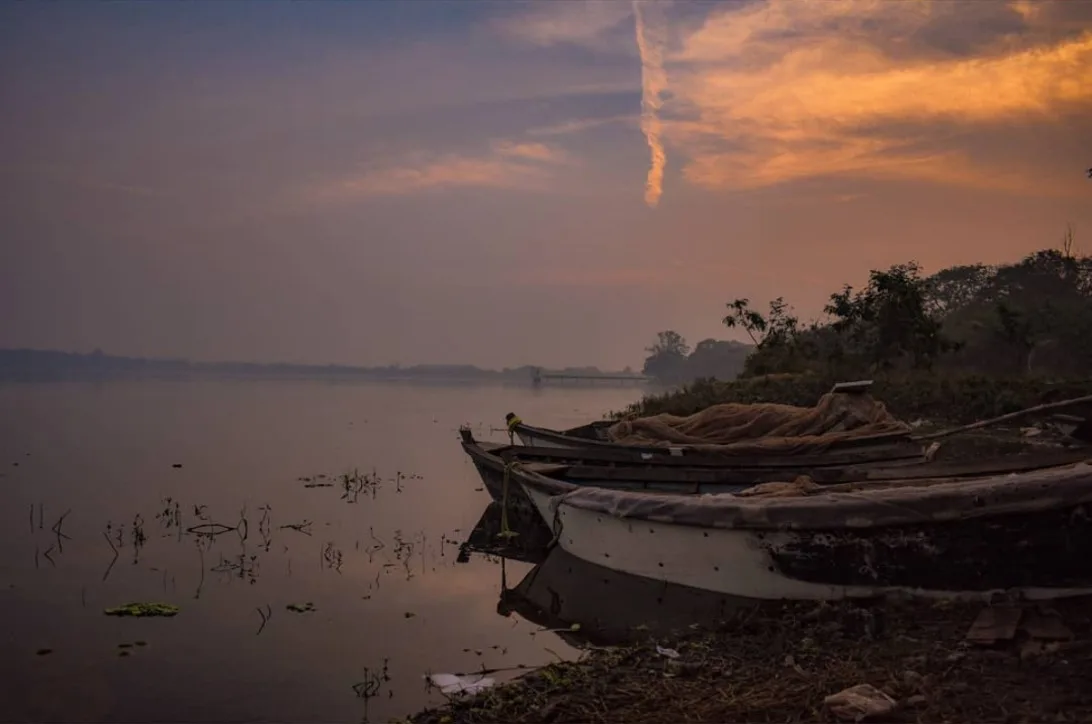 Wooden boats pulled up on the bank of a misty lake under an orange sky